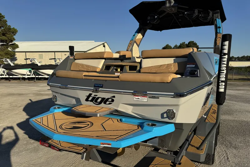 Slide: The Image of 2026 Tigé Ultré 25ZX boat with tan seating and blue accents, parked outdoors. - 3