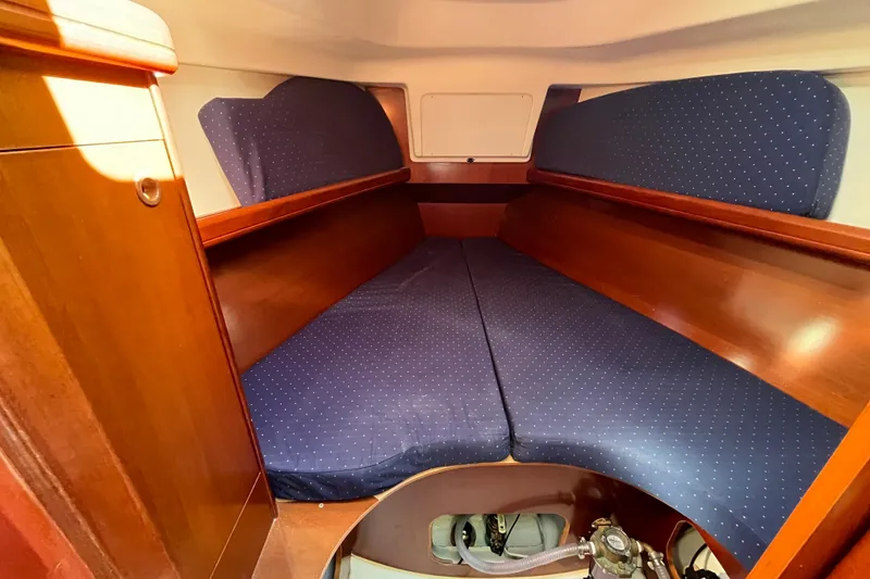 Slide: The Image of 2004 Beneteau 331 yacht cabin with blue cushioned V-berth and wooden interior. - 23