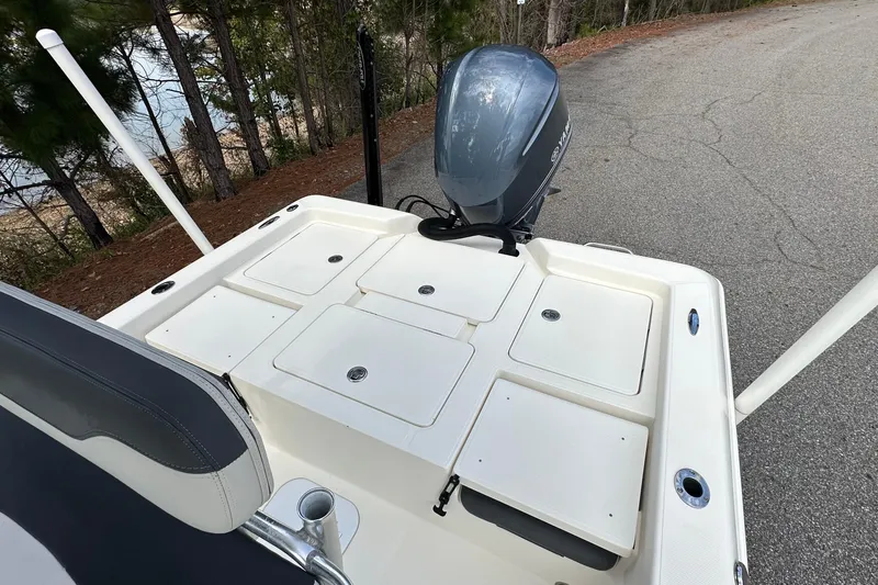 Slide: The Image of 2013 Skeeter SX240 boat deck with storage compartments and outboard motor, parked near trees. - 10