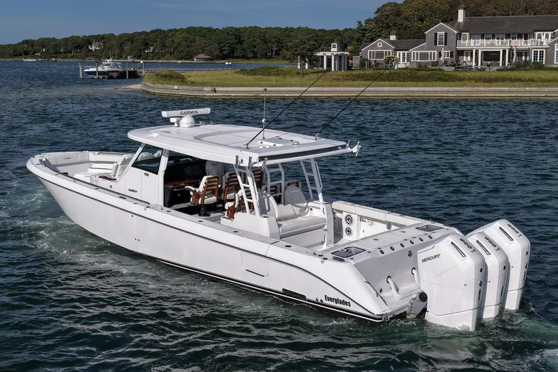 Slide: The Image of 2026 Everglades 455 Center Console boat cruising near a coastal home. - 14