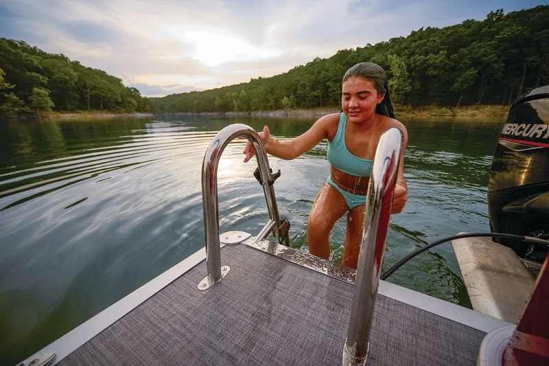 Slide: The Image of Manufacturer Provided Image: Woman climbing onto 2026 Sun Tracker Party Barge 18 DLX in serene lake setting. - 13