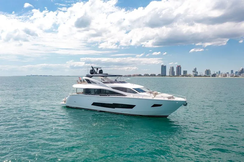 Slide: The Image of 2021 Sunseeker 86 Yacht cruising on open water with city skyline in background. - 2