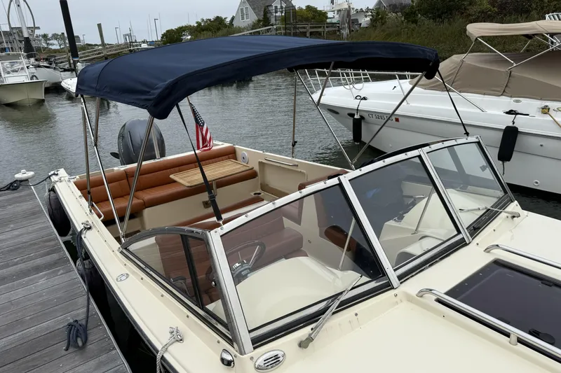 Slide: The Image of 2015 Rossiter 23 boat interior with leather seating, wooden table, and American flag at marina. - 23