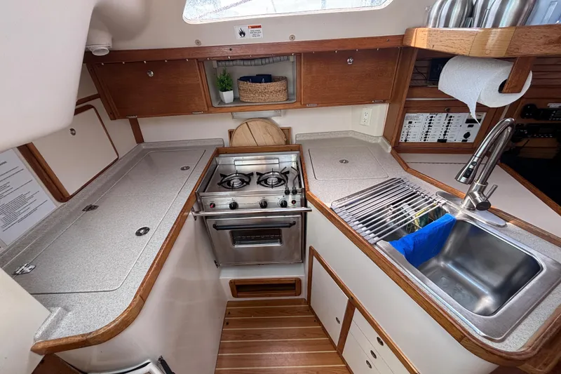 Slide: The Image of Compact kitchen in a 2006 Catalina 320 sailboat with stove, sink, and wooden cabinetry. - 27