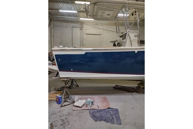 Slide: The Image of Custom Dominion 23 boat, 2023 model, in a workshop setting, blue and white hull. - 11