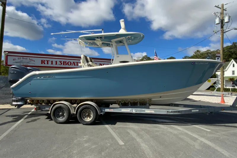 The Image of 2021 Cobia 280 Center Console boat on trailer at dealership, under blue sky. - 1