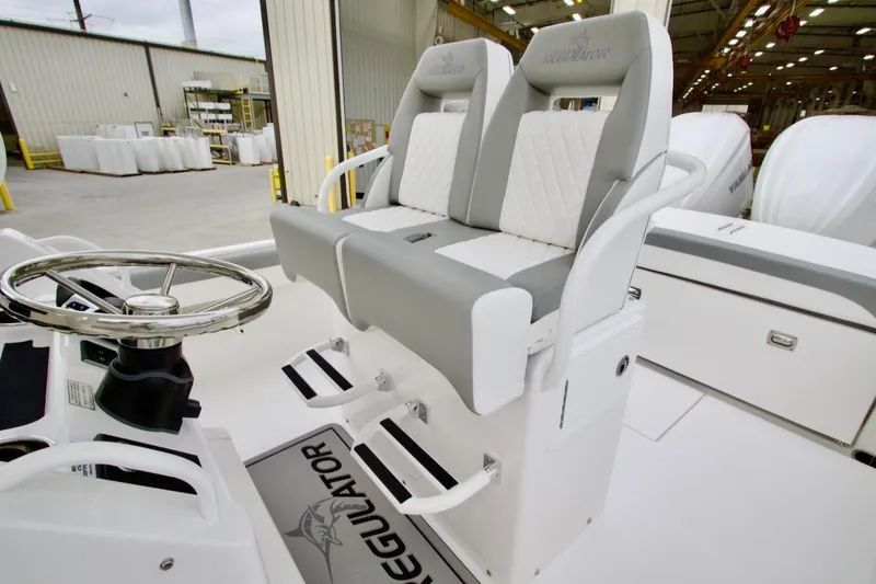 Slide: The Image of 2026 Regulator 25 boat helm with dual seats and steering wheel in a warehouse setting. - 12