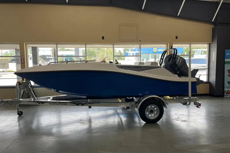 Slide: The Image of 2026 Starcraft SV 16 OB boat on trailer in showroom, blue and white design. - 3