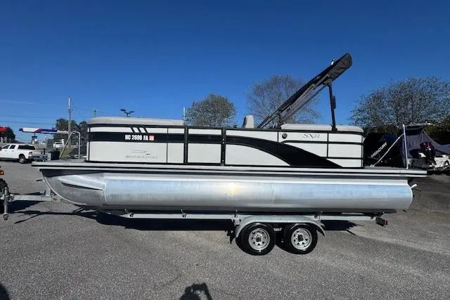 Slide: The Image of 2023 Bennington 22SX pontoon boat on trailer, parked outdoors under clear blue sky. - 2