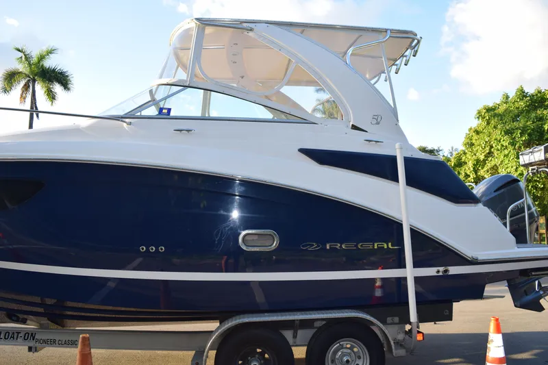 Slide: The Image of 2021 Regal 26 XO boat on trailer, blue and white design, sunny day. - 233