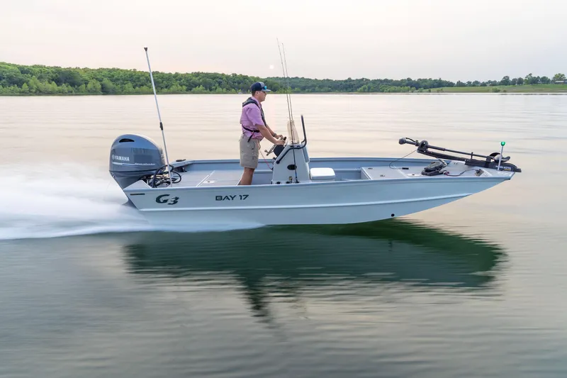 Slide: The Image of 2026 G3 Bay 17 boat cruising on a calm lake with lush green shoreline. - 16