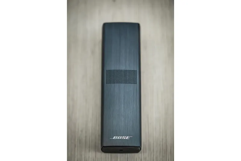 Slide: The Image of Bose remote control on wooden surface, sleek design, top view. - 56