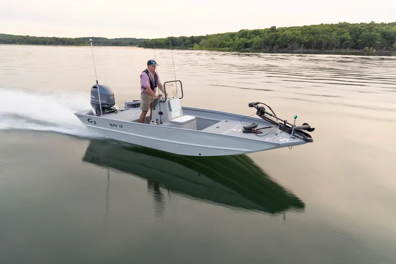 Slide: The Image of 2026 G3 Bay 17 boat cruising on a calm lake with a person steering. - 2