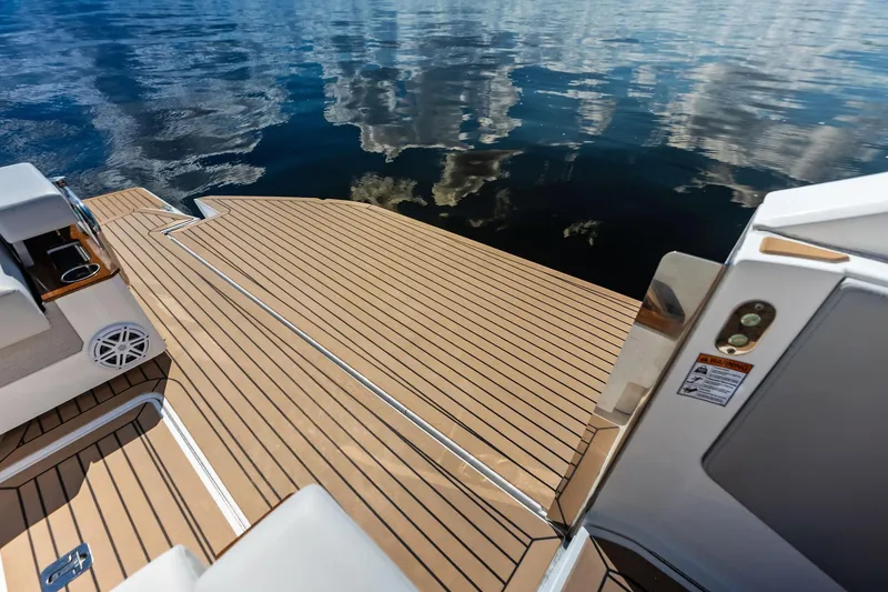 Slide: The Image of 2024 Tiara Yachts 48 LS swim platform with teak decking, reflecting sky and clouds on water. - 27