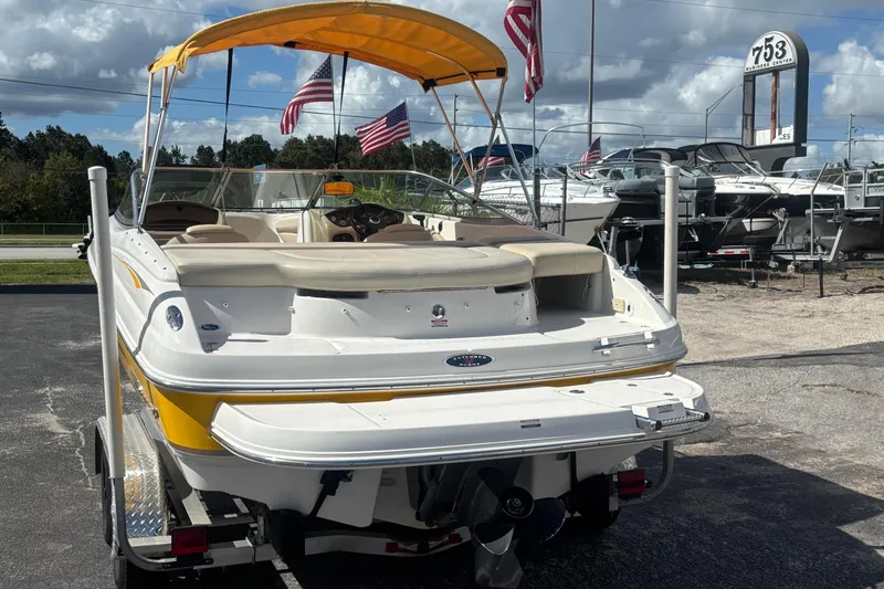 Slide: The Image of 2004 Chaparral 210 SSi boat with yellow accents, parked on a trailer, under a sunny sky. - 2