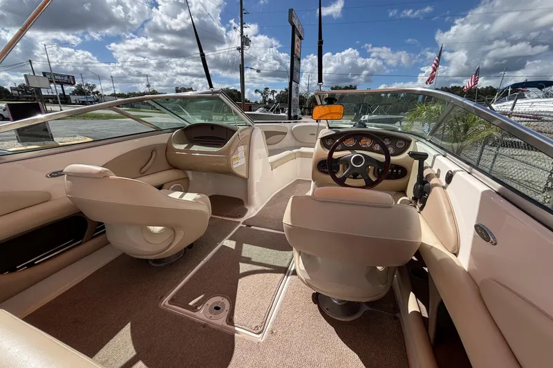 Slide: The Image of 2004 Chaparral 210 SSi boat interior with beige seating and dashboard under a sunny sky. - 33