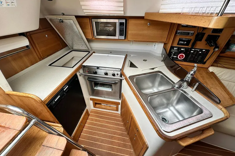 Slide: The Image of 2008 Catalina 320 yacht kitchen with stove, sink, microwave, and wooden cabinetry. - 62