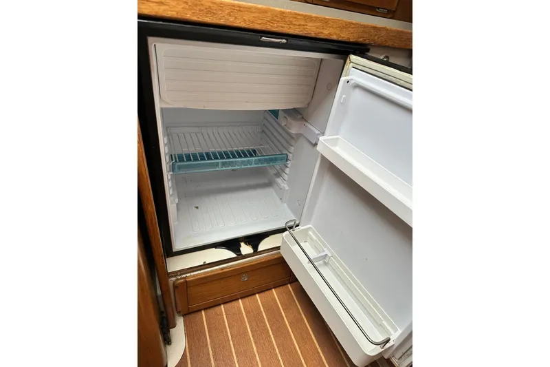 Slide: The Image of Open refrigerator inside a 2008 Catalina 320 sailboat, featuring wooden flooring and shelving. - 71