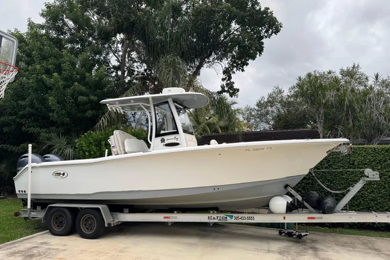 The Image of 2021 Sea Hunt Gamefish 25 boat on trailer, parked outdoors with lush greenery background. - 0