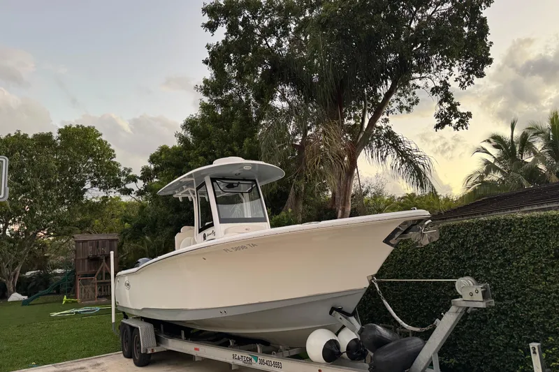 Slide: The Image of 2021 Sea Hunt Gamefish 25 boat on trailer, surrounded by lush greenery. - 19