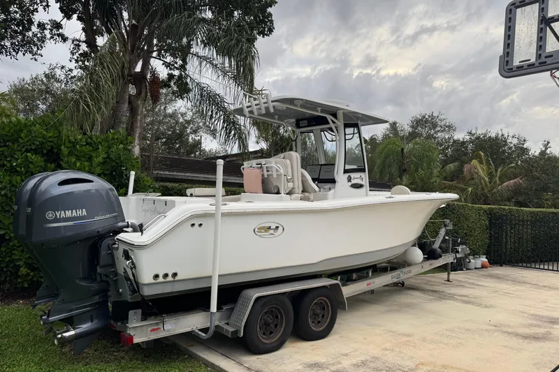 Slide: The Image of 2021 Sea Hunt Gamefish 25 boat on trailer with Yamaha engine, surrounded by lush greenery. - 2