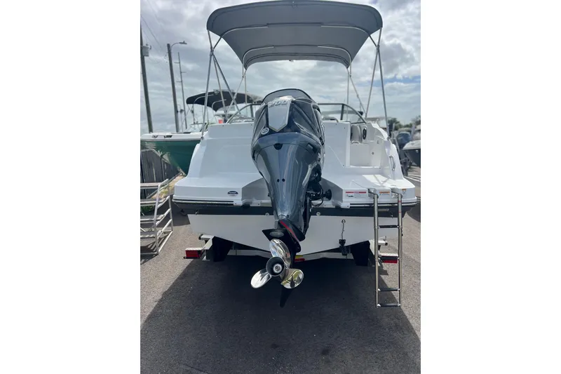 Slide: The Image of 2026 Hurricane SunDeck 235 OB boat with outboard motor and ladder, docked under cloudy sky. - 2