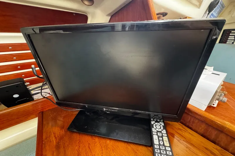 Slide: The Image of Flat-screen TV and remote on wooden surface inside 1982 Pearson 323 boat cabin. - 64