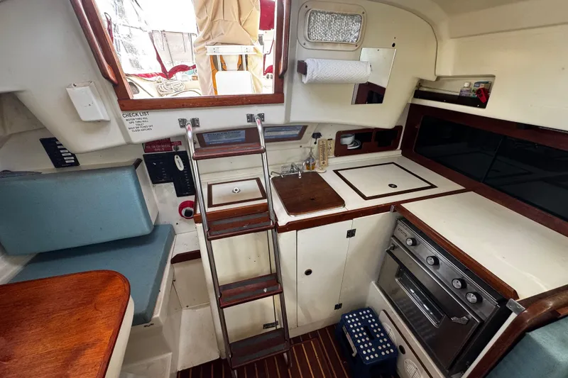 Slide: The Image of 1982 Pearson 323 yacht interior with compact kitchen, wooden accents, and ladder access. - 73