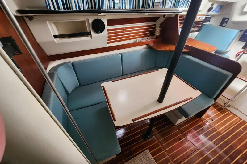 Slide: The Image of 1982 Pearson 323 sailboat interior with blue cushioned seating and wooden table. - 28