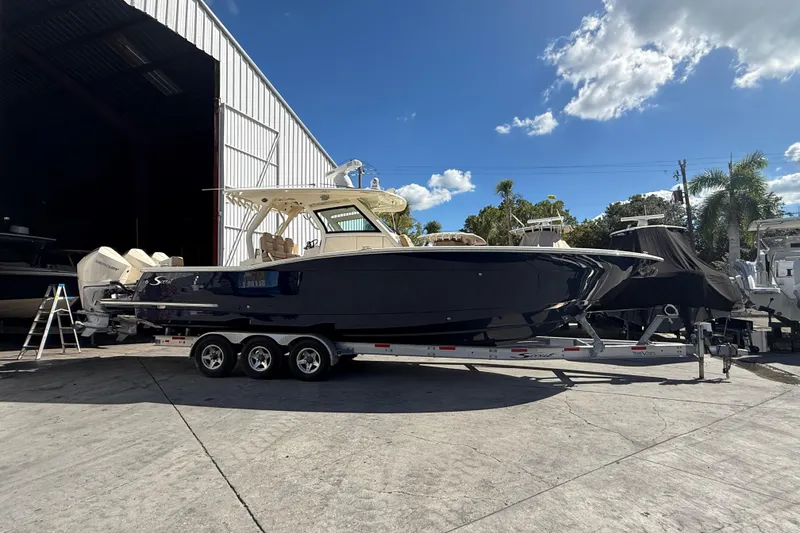 The Image of 2022 Scout 355 LXF boat on trailer outside a storage facility under a clear blue sky. - 0