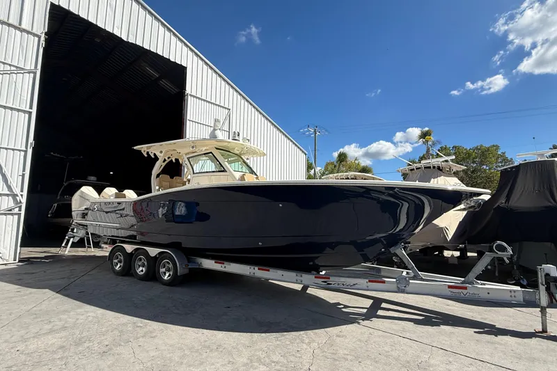 Slide: The Image of 2022 Scout 355 LXF boat on trailer outside storage facility under blue sky. - 3