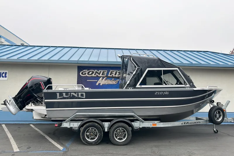 The Image of 2026 Lund 210 Heavy Gauge boat on trailer, parked outside a marine store. - 0