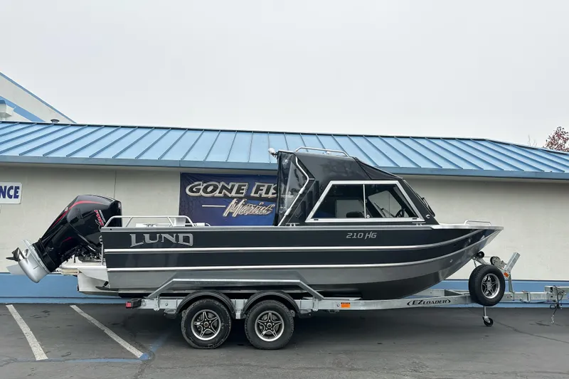 Slide: The Image of 2026 Lund 210 Heavy Gauge boat on trailer, parked outside a marine store. - 34