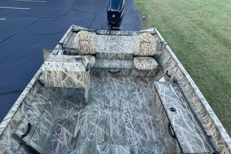 Slide: The Image of 2026 Lowe Roughneck 2070SC boat with camouflage interior, parked on grass and pavement. - 13