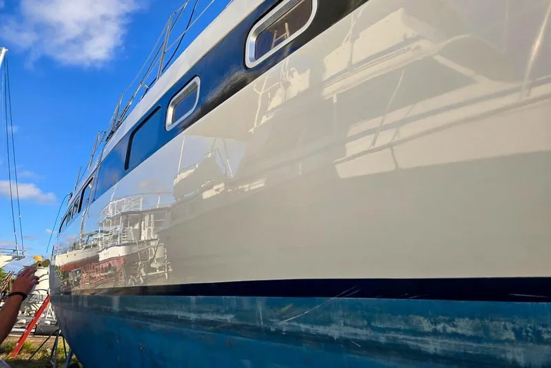 Slide: The Image of Polished hull of a 2006 Dolphin 460 sailboat reflecting nearby boats under a clear blue sky. - 60