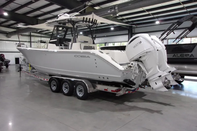 The Image of 2026 Cobia 305 Center Console boat with dual engines on a trailer in a showroom. - 1