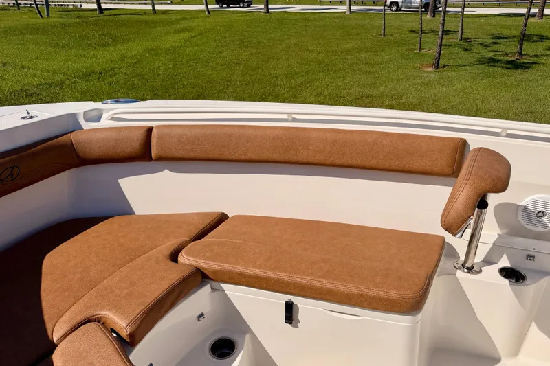 Slide: The Image of 2015 Sailfish 290 CC boat interior with tan cushioned seating and green grass background. - 11