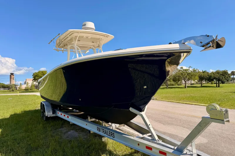 Slide: The Image of 2015 Sailfish 290 CC boat on trailer, parked on grass under clear blue sky. - 3