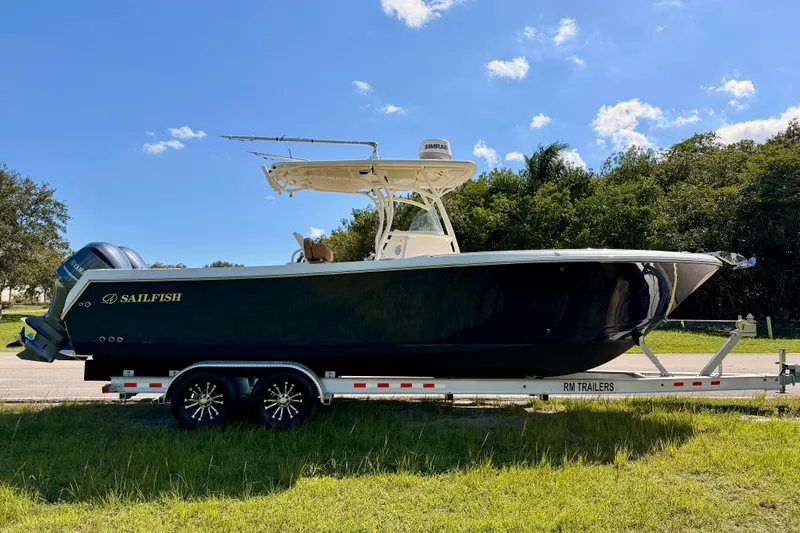 Slide: The Image of 2015 Sailfish 290 CC boat on trailer, parked on grass under blue sky. - 4