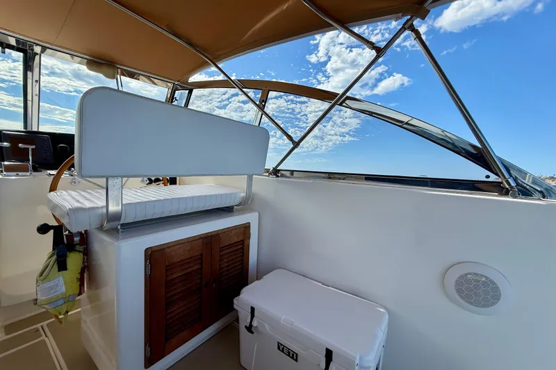 Slide: The Image of 1999 Legacy 40 boat interior with helm seat, wooden cabinet, and cooler under a clear sky. - 49