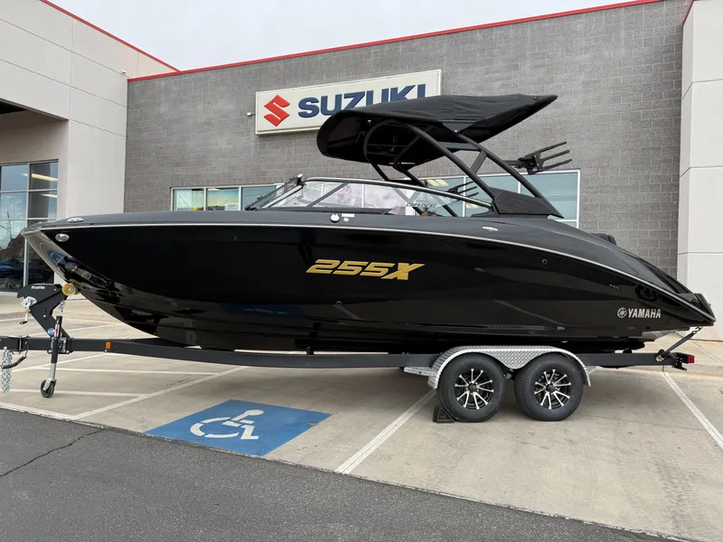 The Image of 2025 Yamaha Boats 255XD in black, displayed on a trailer outside a Suzuki dealership. - 0