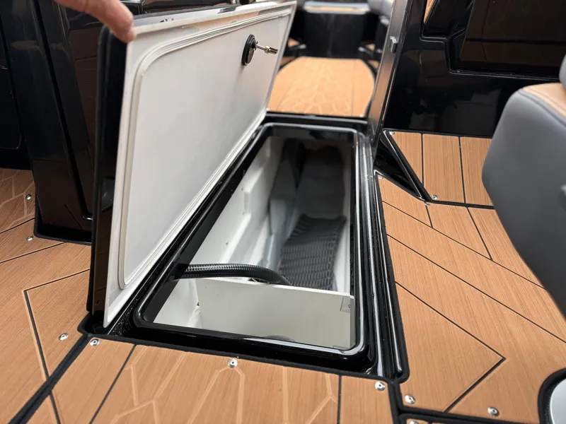 Slide: The Image of 2025 Yamaha Boats 255XD storage compartment with open hatch on wooden deck. - 60