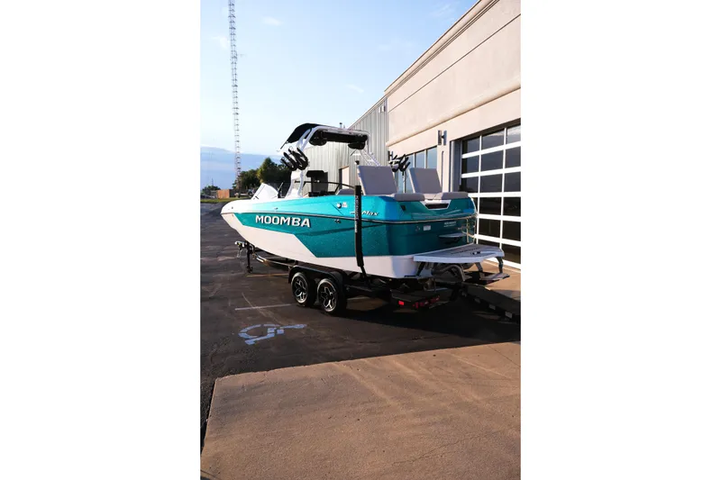 Slide: The Image of 2026 Moomba Max boat in teal, parked on a trailer near a building. - 11