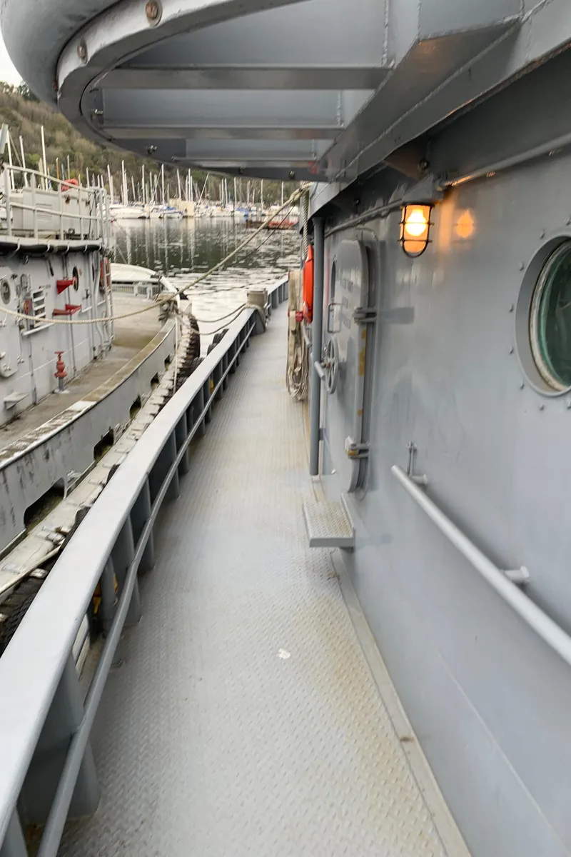 Slide: The Image of 1955 L-T 100 Steel Army Tugboat deck with railing and porthole, docked at marina. - 8