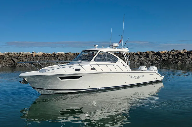 Slide: The Image of 2024 Pursuit OS 325 Offshore boat on calm water near rocky shore. - 2