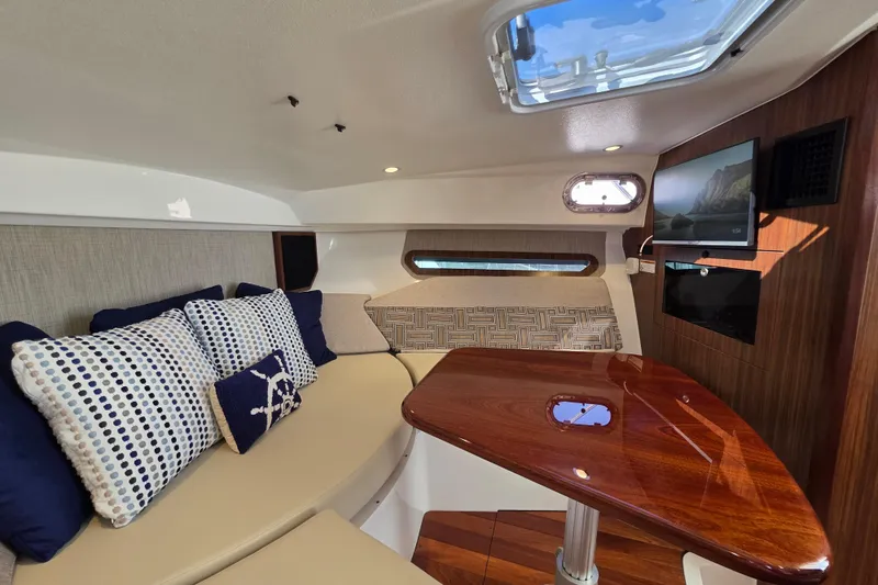 Slide: The Image of 2024 Pursuit OS 325 Offshore cabin with plush seating, wooden table, and mounted TV. - 58