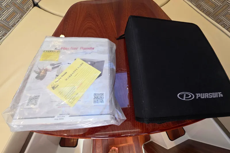 Slide: The Image of 2024 Pursuit OS 325 Offshore manuals and warranty card on wooden table. - 63