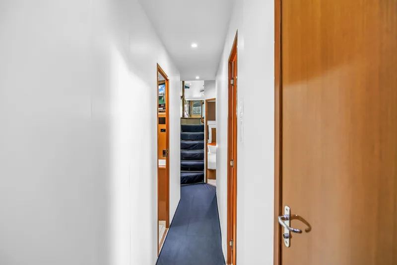 Slide: The Image of Hallway inside 1999 Viking 72 Enclosed Bridge yacht, featuring wooden doors and carpeted stairs. - 52