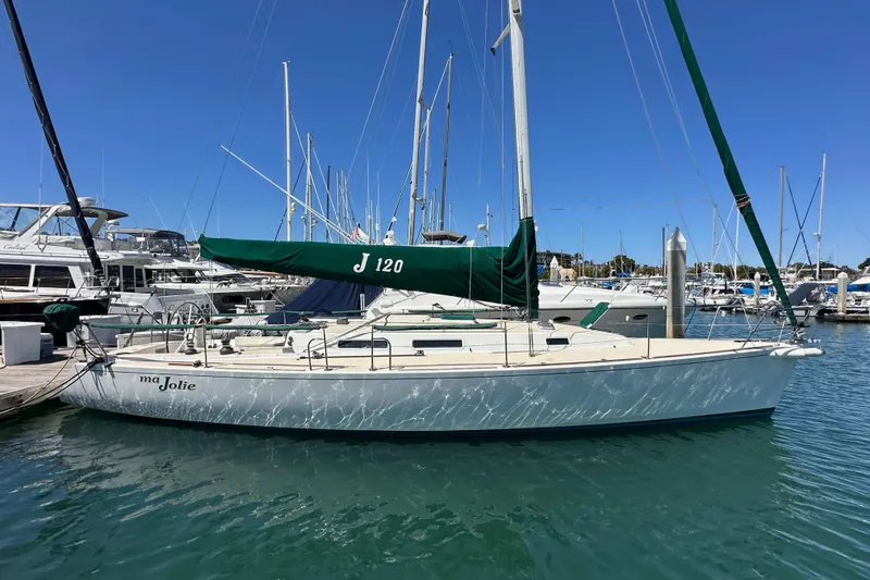 The Image of 1996 J Boats J/120 sailboat docked in marina, clear blue sky, green sail cover. - 0