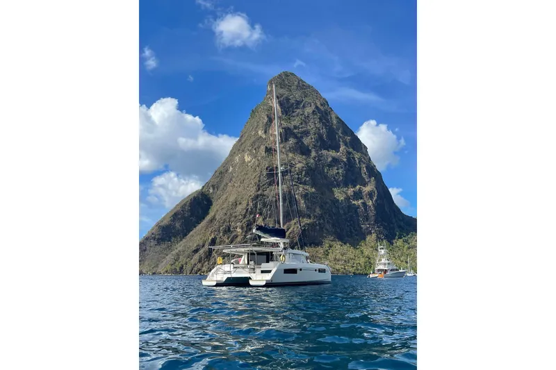 Slide: The Image of Leopard 45 catamaran sailing near a towering mountain under a clear blue sky. - 111